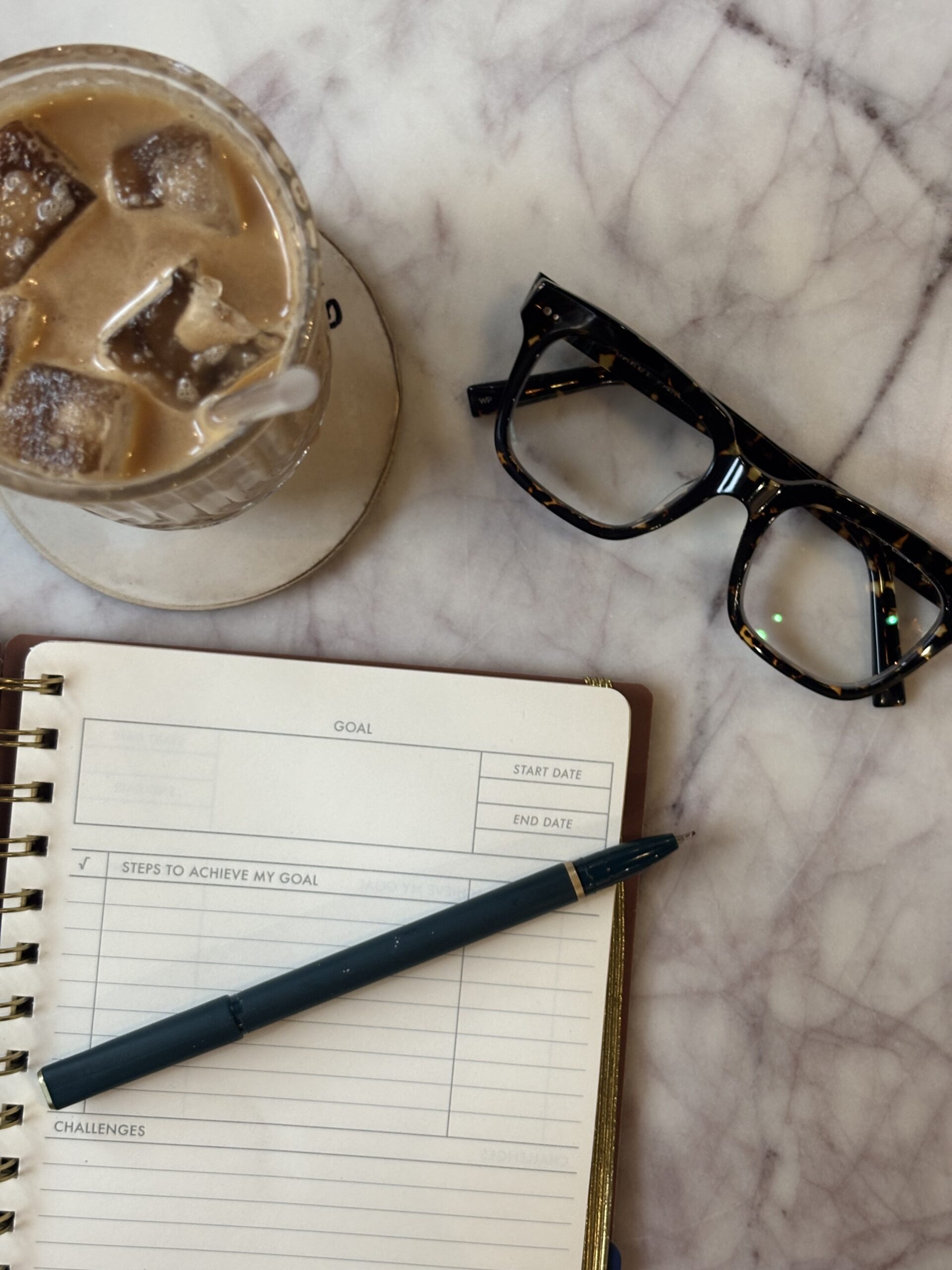 overhead view of a notebook, iced coffee, and glasses to begin rebuilding life after quitting drinking