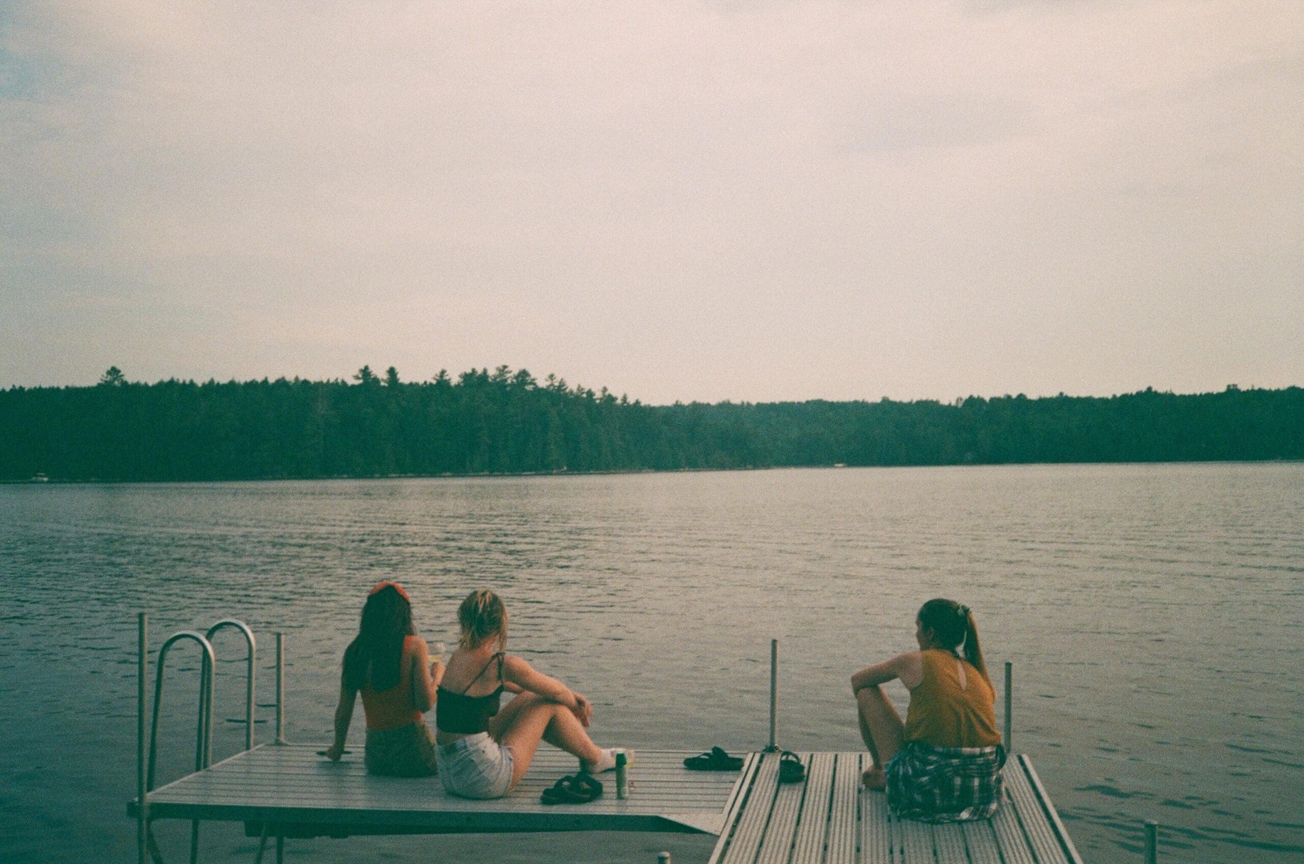 Two women sitting side by side on a dock overlooking the water, representing the deep connection and support found in sober friendships