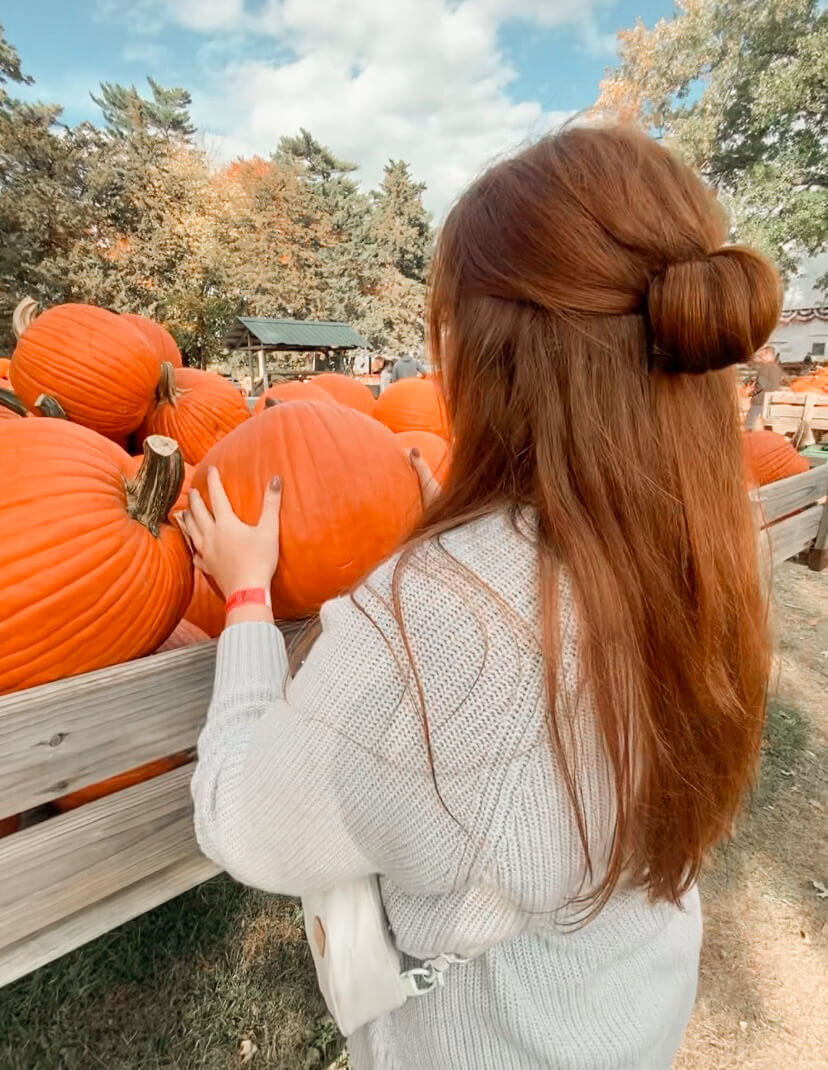 Woman picking a pumpkin from a vintage truck at a fall pumpkin patch during a cozy Sober October afternoon.