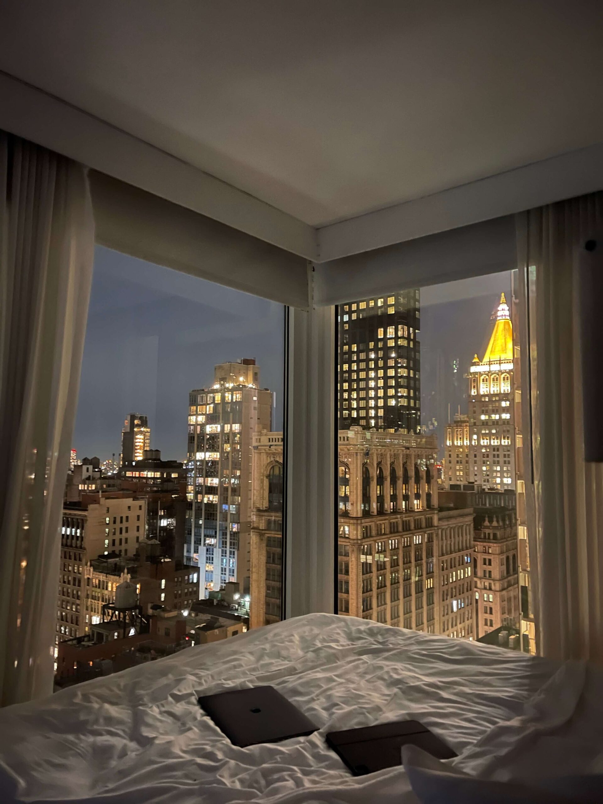 A luxurious bed with floor-to-ceiling windows overlooking the New York City skyline, representing the intentional, deeply rested sober lifestyle every alcohol-free woman deserves.