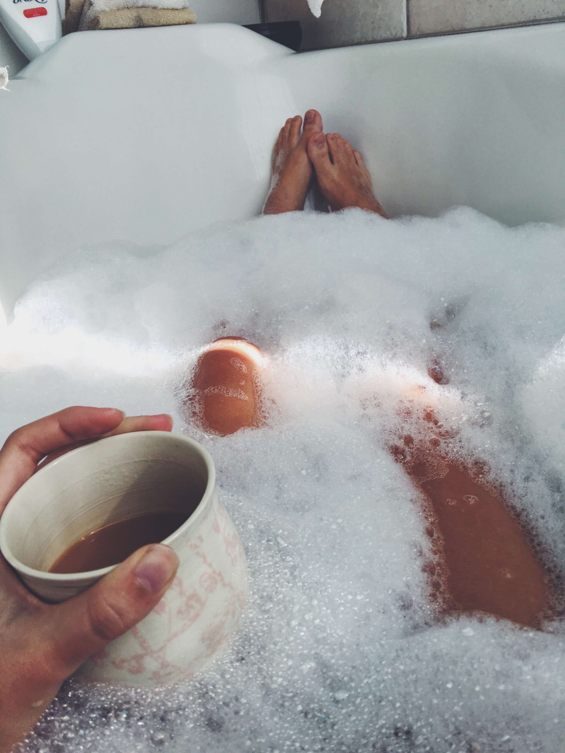 Person relaxing in a bubble bath with a mug of tea as part of a calming nervous system self-care routine